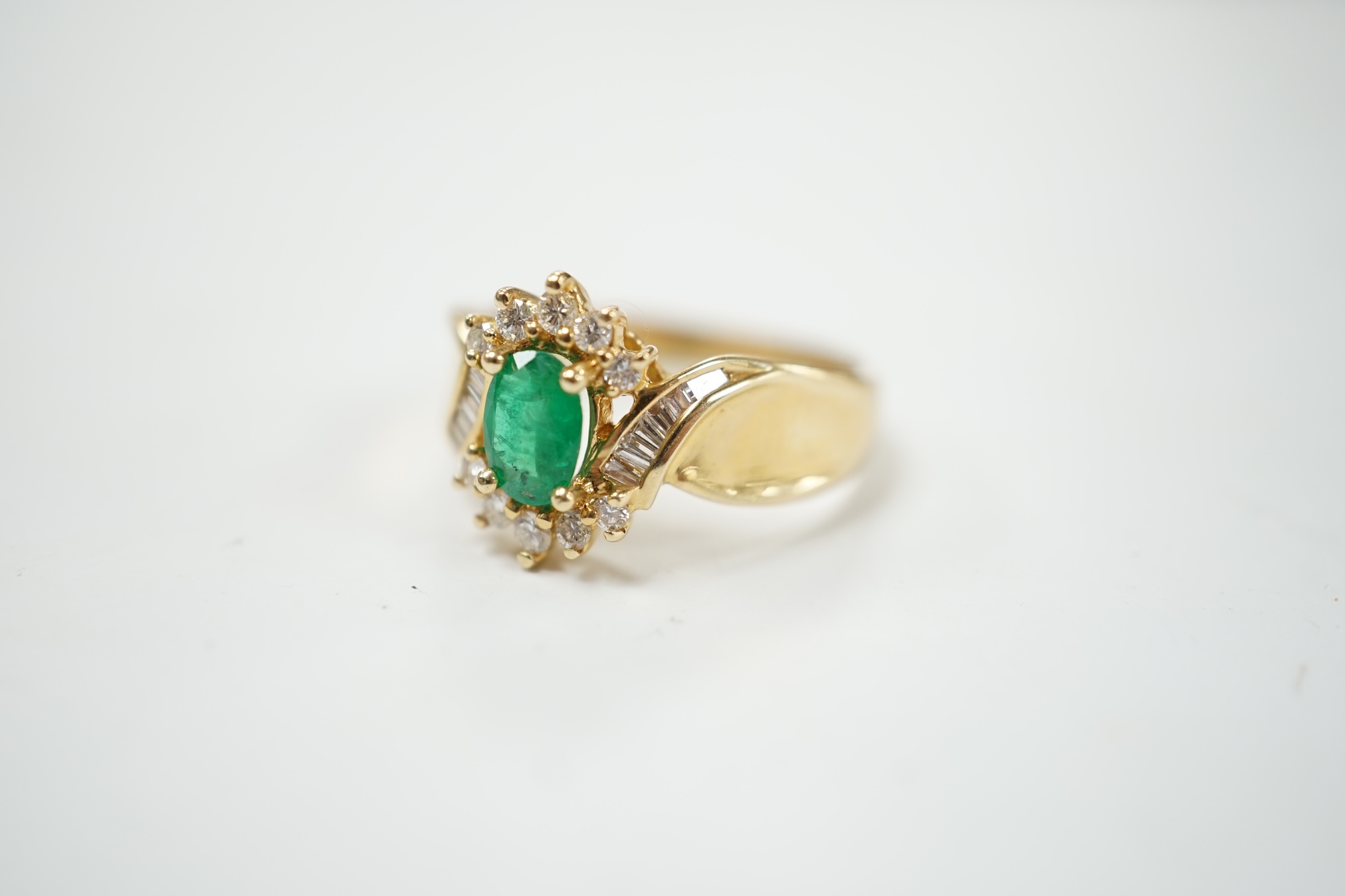A modern 14k, emerald and diamond cluster set ring, with baguette cut diamond set shoulders, size Q, gross weight 4.9 grams. Condition - fair